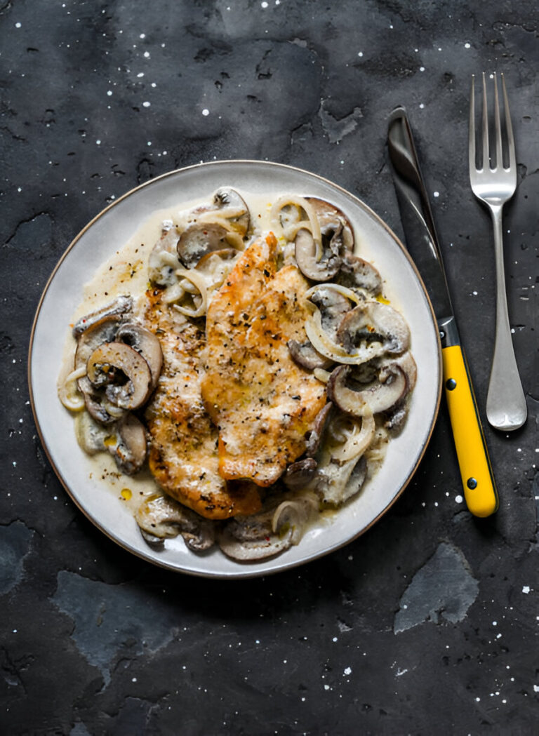 A plate of creamy mushroom and chicken dish with onions on a dark background.