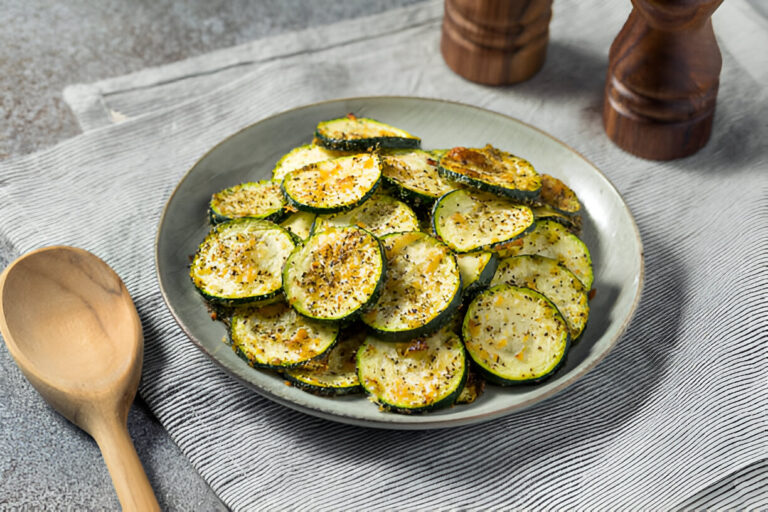 A plate of crispy zucchini chips garnished with herbs, with a wooden spoon and salt shakers in the background.