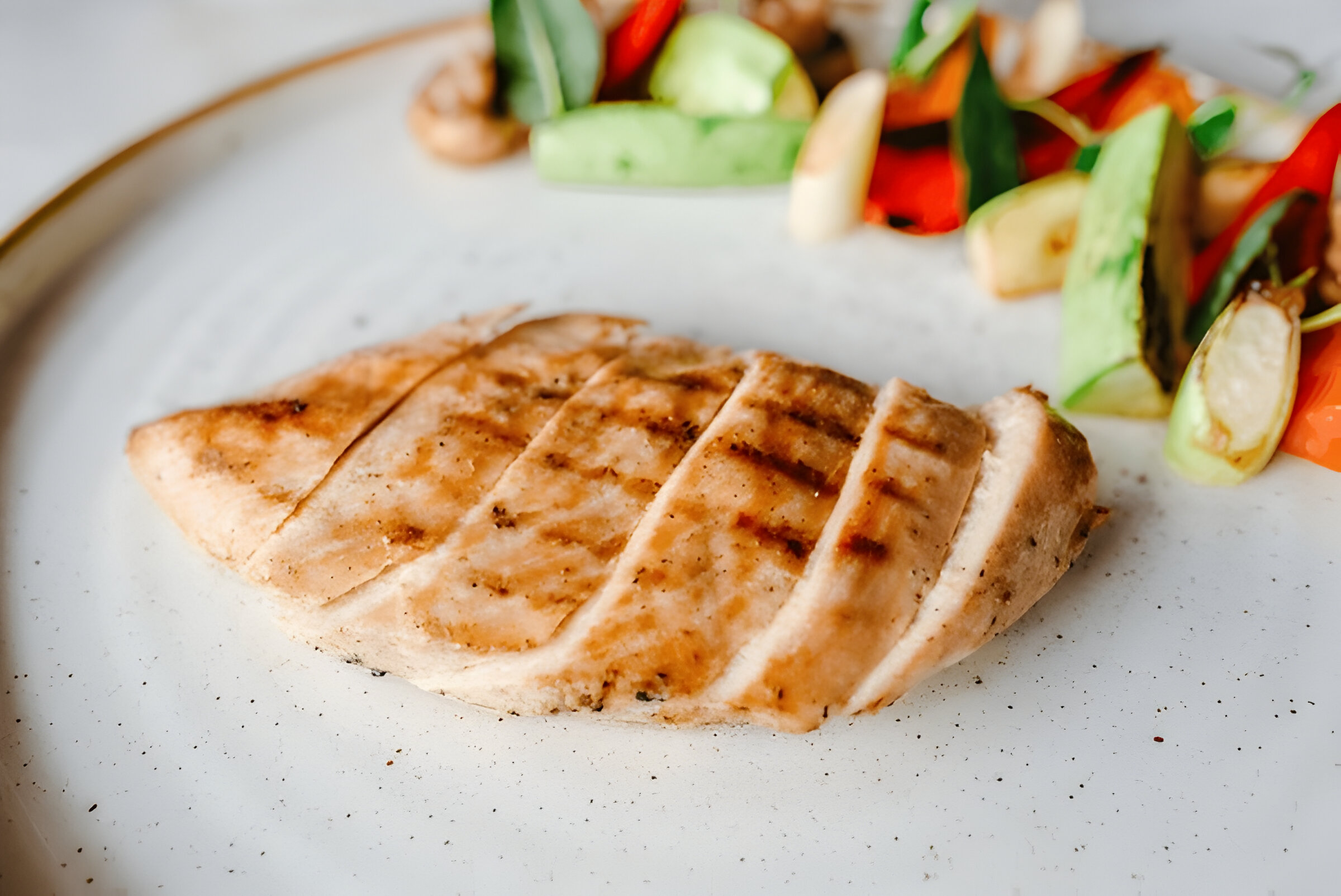 Grilled chicken breast served with colorful sautéed vegetables on a white plate