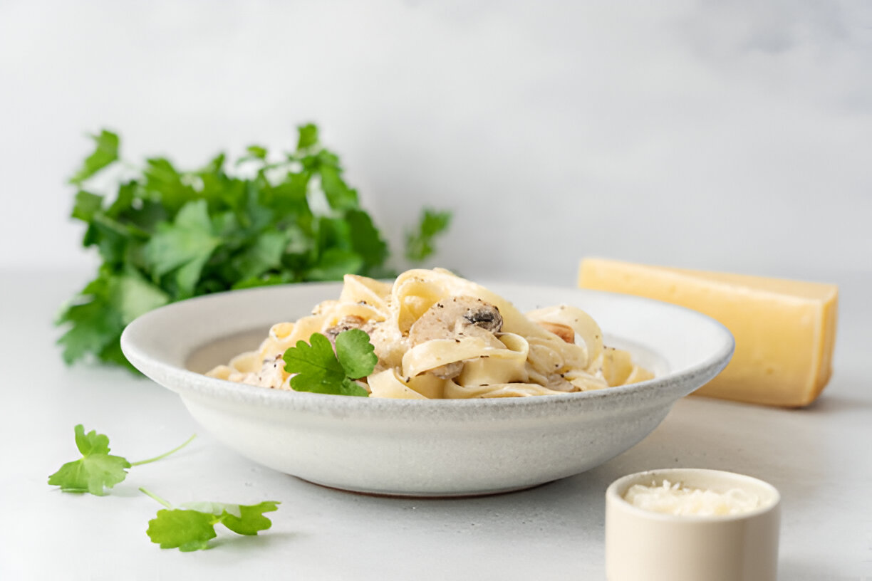 A bowl of creamy fettuccine pasta garnished with fresh cilantro, accompanied by cheese and a small cup of grated cheese.