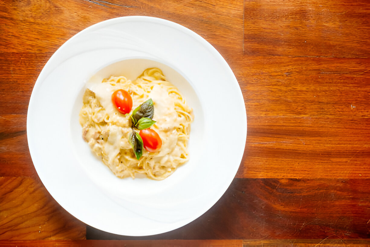 Creamy pasta with cherry tomatoes and basil in a white bowl on a wooden table.