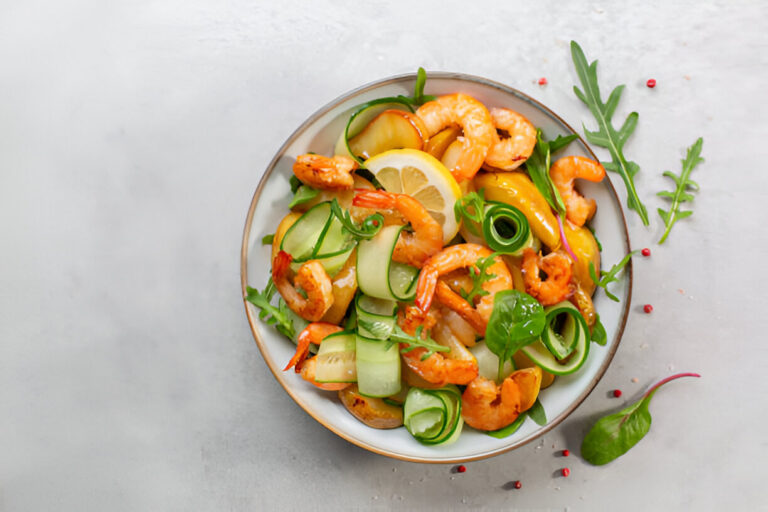 A vibrant shrimp salad with cucumber, yellow peppers, and lemon slices in a bowl.