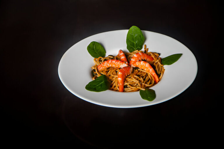 A plate of shrimp pasta with spinach on a dark background.