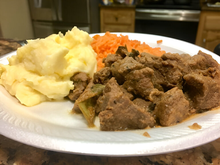 A plate of food featuring mashed potatoes, shredded carrots, and tender meat chunks in gravy.