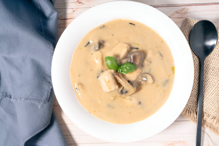 Creamy mushroom soup garnished with fresh basil leaves, served in a white bowl on a wooden table.