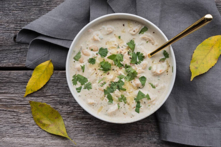 A bowl of creamy soup garnished with fresh cilantro and served with a golden spoon on a textured wooden surface.