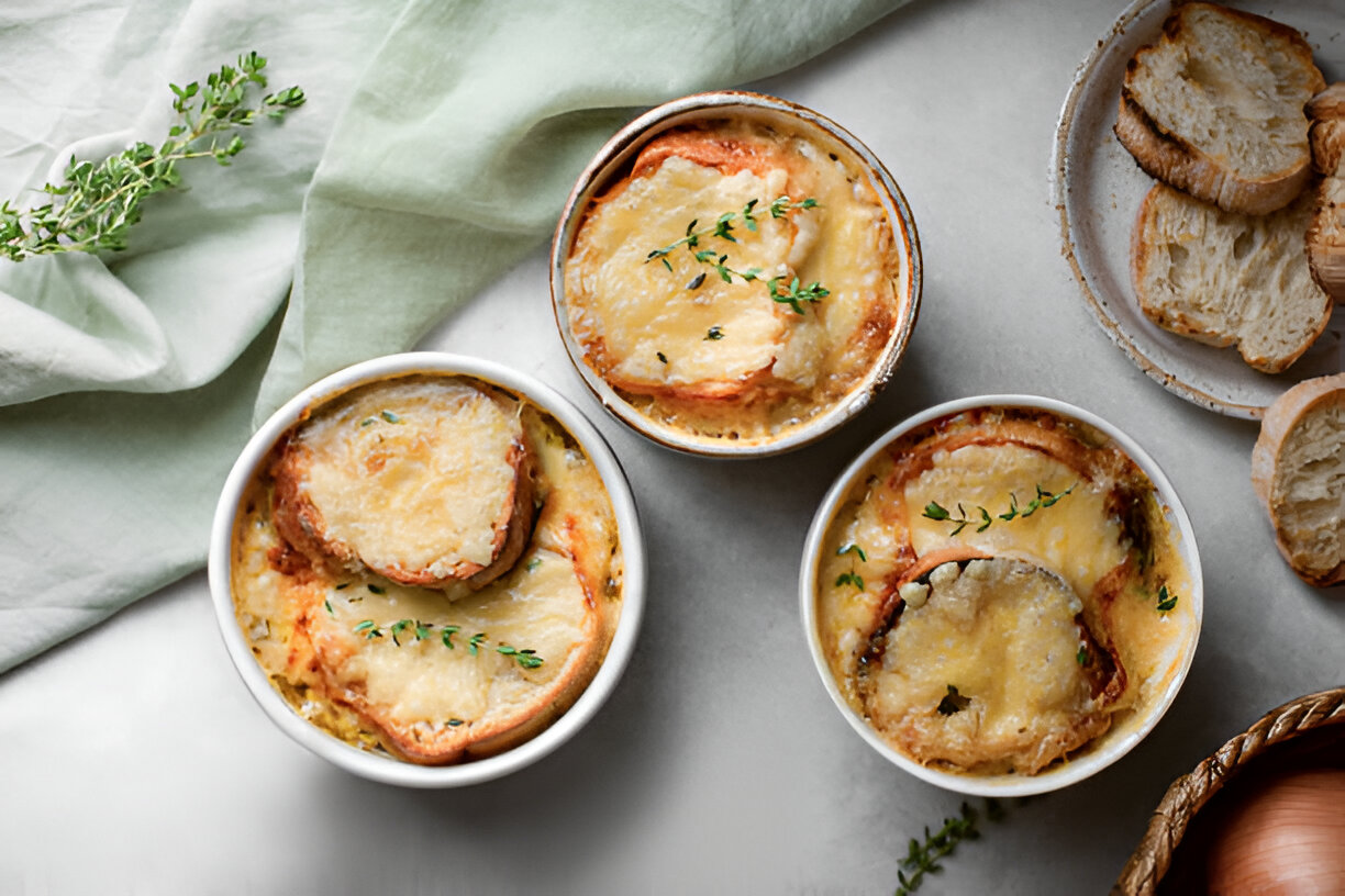 Three individual servings of French onion soup with melted cheese and herbs, served in white ramekins.