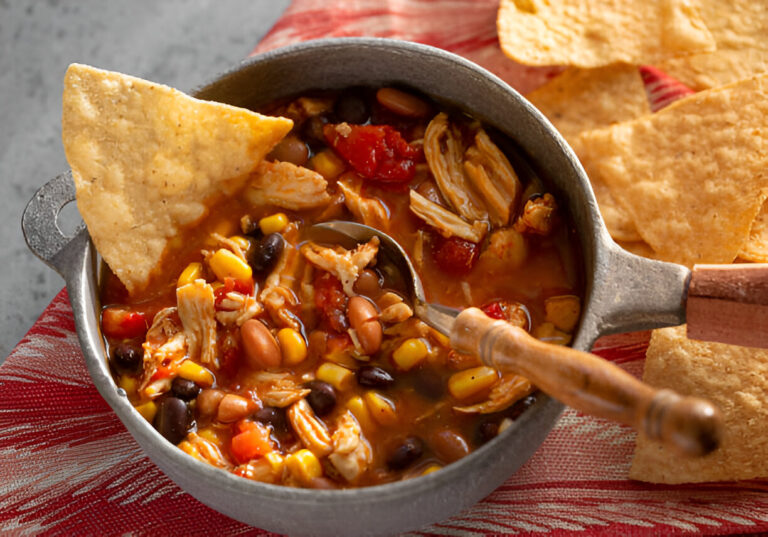 A pot of colorful chicken chili with black beans, corn, and diced tomatoes, accompanied by tortilla chips.