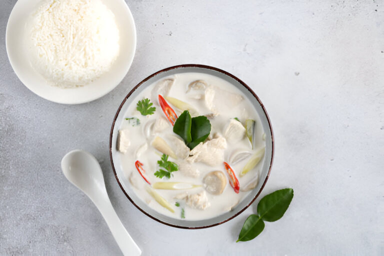 A bowl of creamy chicken soup with herbs and spices accompanied by a plate of steamed rice.