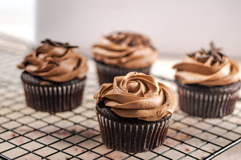 A close-up view of chocolate cupcakes with swirled frosting on a cooling rack.