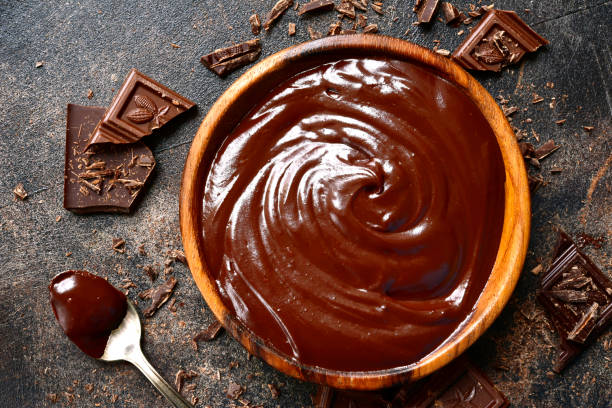 A bowl of rich chocolate ganache with chocolate pieces scattered around it.