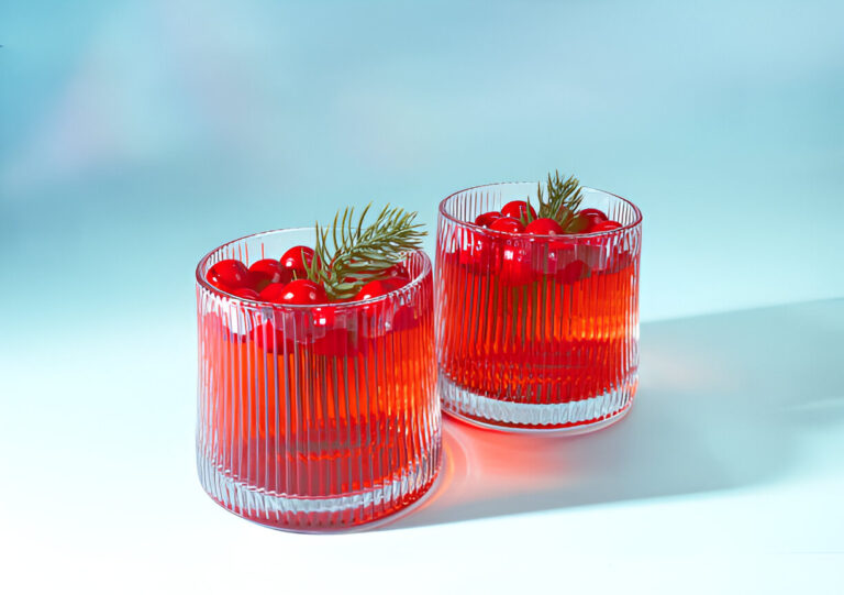 Two glasses filled with a bright red liquid and garnished with cherries and a sprig of greenery.