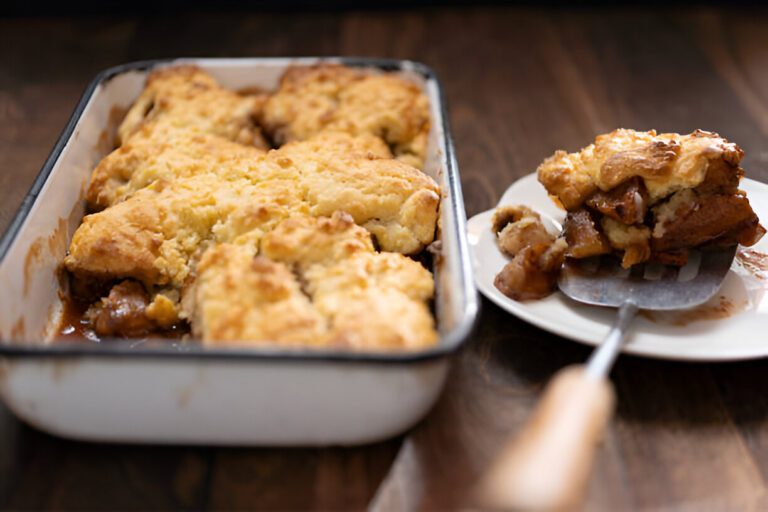 A freshly baked cobbler in a dish, with a serving on a plate next to it.