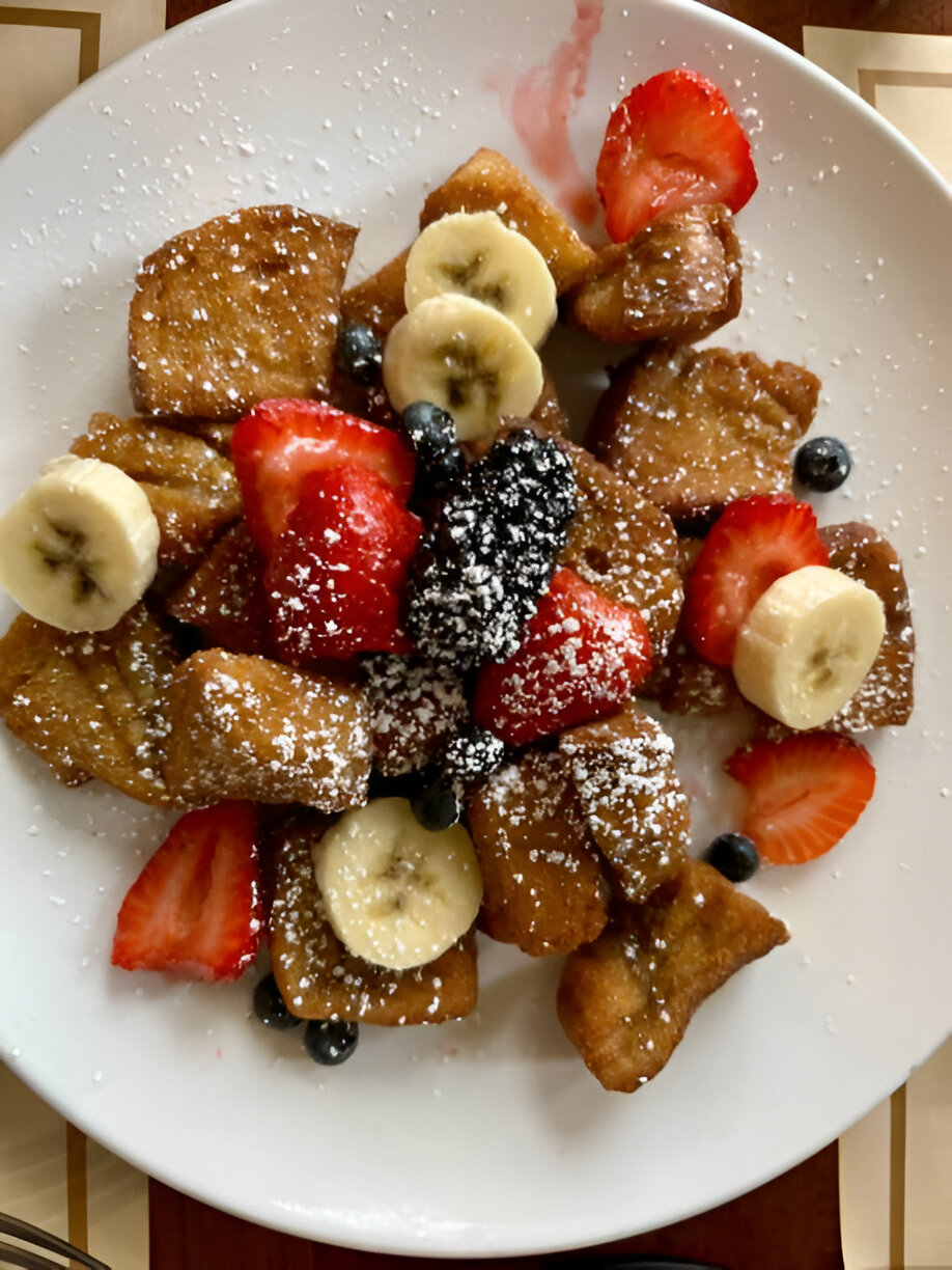 Delicious plate of French toast pieces topped with strawberries, bananas, blueberries, and powdered sugar.