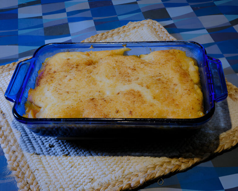 A baked casserole dish with a golden, crispy top resting on a woven placemat.