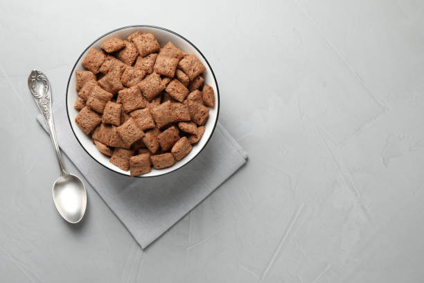 A bowl of chocolate cereal pieces on a textured gray surface