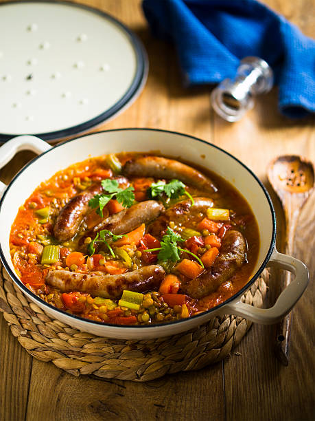 A pot of sausage stew filled with vegetables on a wooden surface.