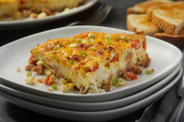 A slice of cheesy breakfast casserole with green onions on a white plate, accompanied by toasted bread.