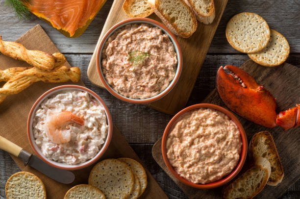 A selection of seafood spreads in bowls, including shrimp, crab, and salmon, served with various crackers and bread on a wooden surface.