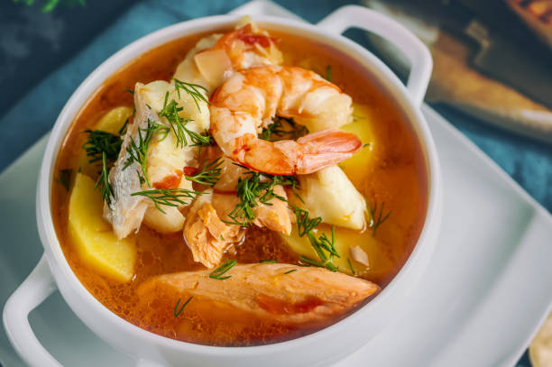 A bowl of seafood soup with shrimp, fish, and potatoes garnished with herbs.