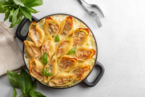 A delicious dish of stuffed pasta shells arranged in a black skillet with fresh basil leaves around it.