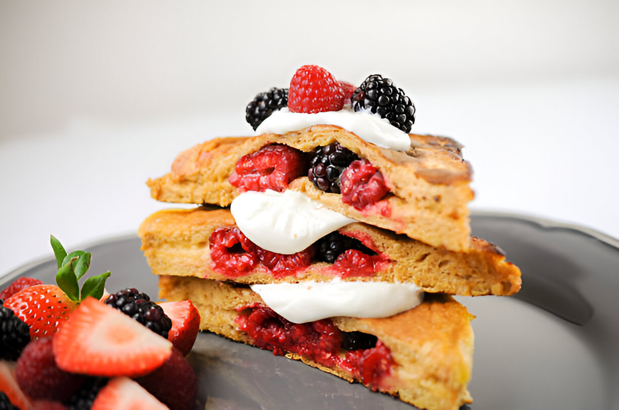 Three layers of pancakes filled with raspberries and blackberries, garnished with whipped cream and fresh berries.