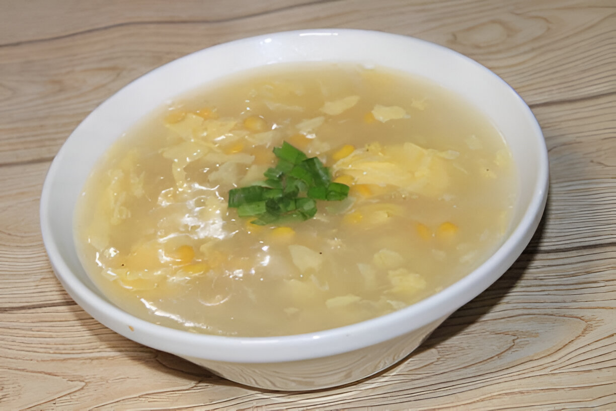 A bowl of soup with corn and cabbage topped with green onions on a wooden surface.