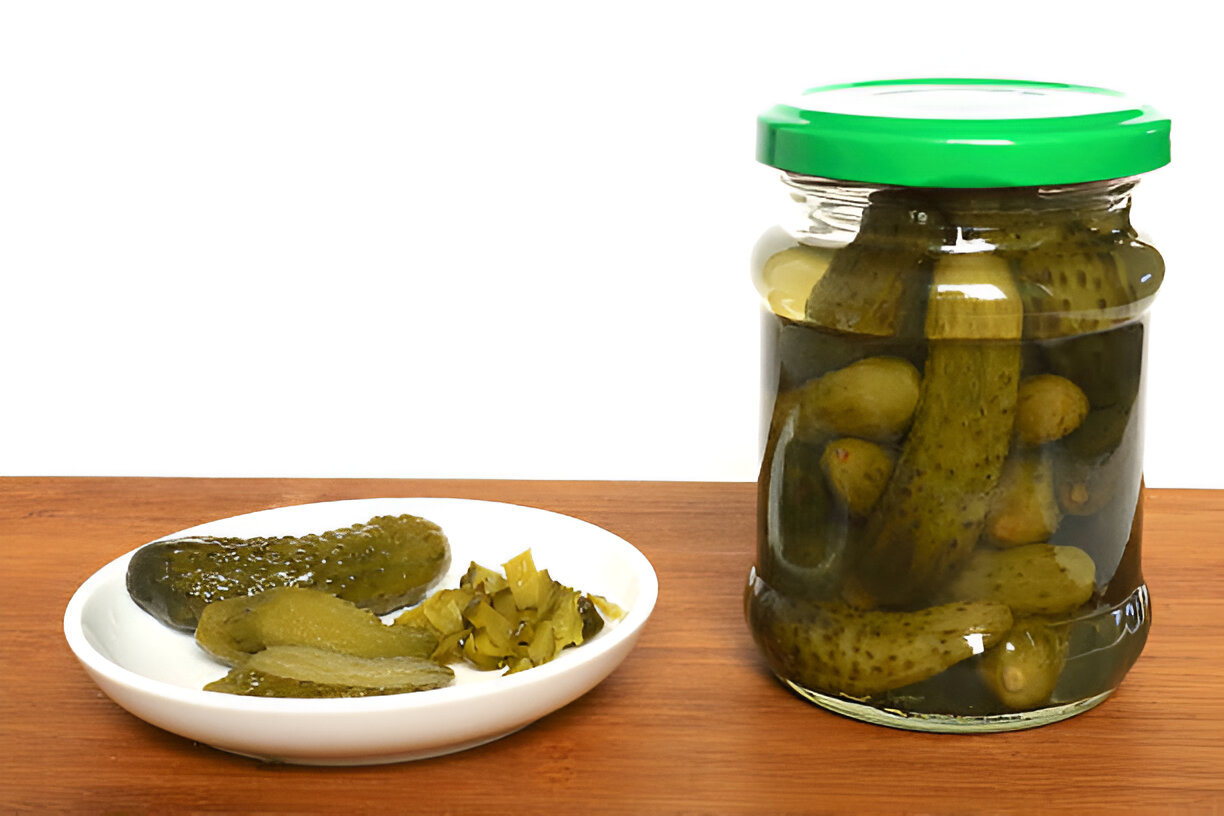 A jar of pickles with some pickles on a plate beside it.