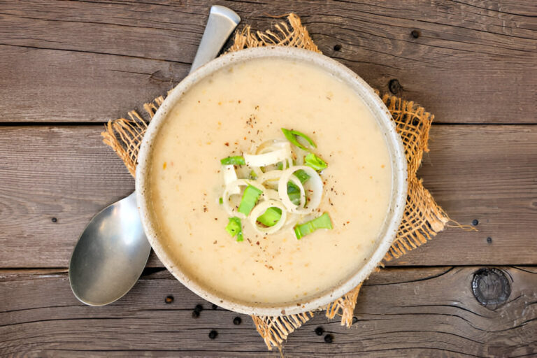 A bowl of creamy soup topped with sliced green onions on a rustic wooden table.