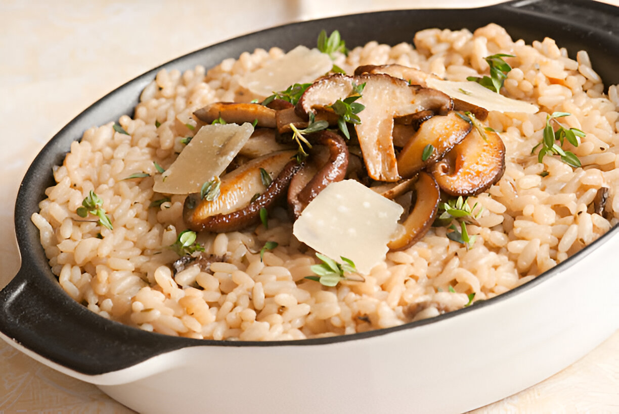 A dish of creamy risotto topped with sautéed mushrooms, fresh thyme, and shaved Parmesan cheese.