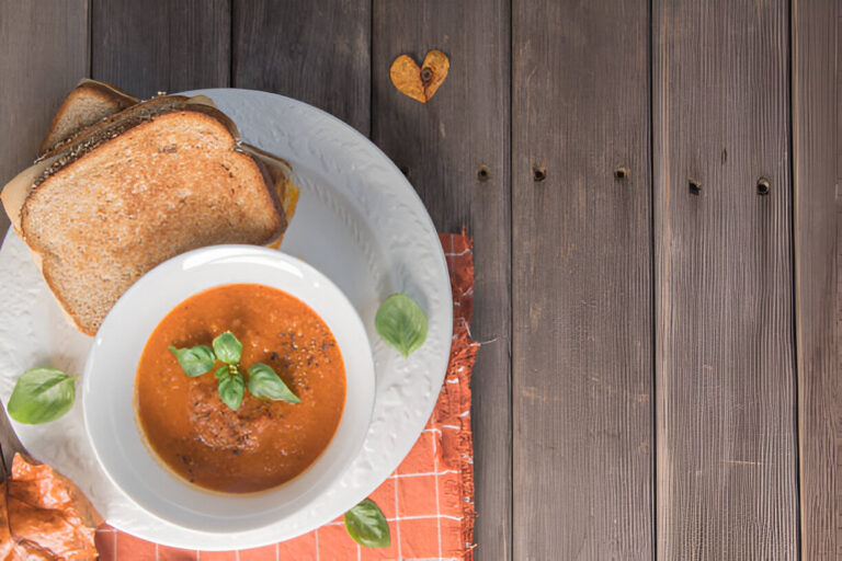 A bowl of tomato soup garnished with basil leaves, accompanied by toasted bread, on a rustic wooden table.