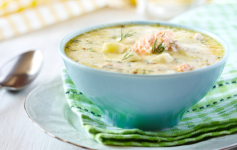 A bowl of creamy salmon soup garnished with fresh dill, sitting on a green striped cloth.