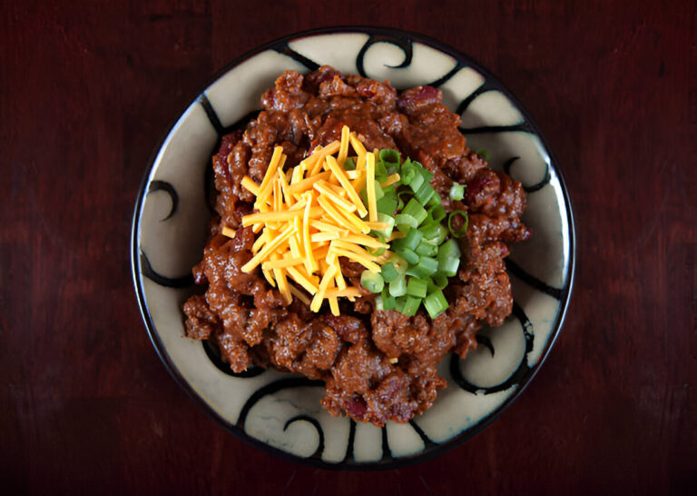 A bowl of hearty chili topped with shredded cheese and chopped green onions.