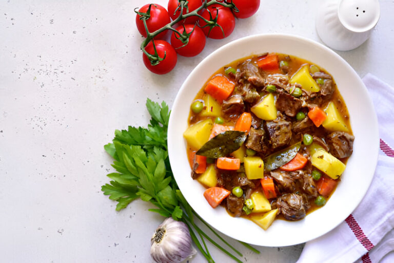 A hearty beef stew with potatoes, carrots, and green peas served in a white bowl, surrounded by fresh ingredients.