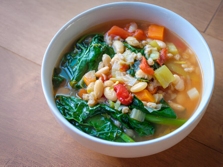 A healthy vegetable soup in a white bowl, featuring greens, beans, and diced vegetables