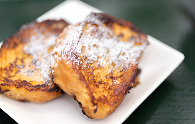 Two slices of golden-brown French toast dusted with powdered sugar on a white plate