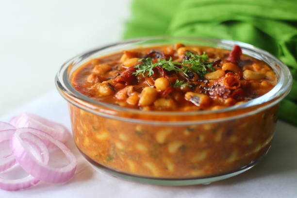 A bowl of flavorful chickpea curry garnished with coriander, served alongside sliced onions.