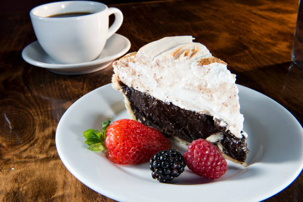 A slice of chocolate pie topped with whipped cream, served with fresh berries and a cup of coffee in the background.