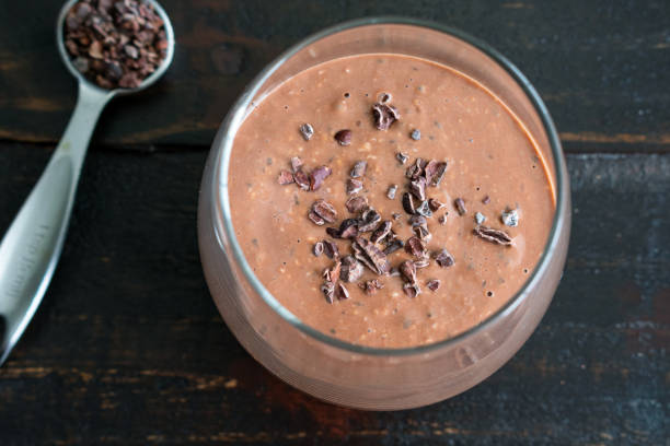 A glass of chocolate smoothie topped with cacao nibs, placed on a wooden surface.