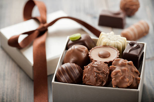 A beautifully arranged box of assorted chocolates with a ribbon, showcasing various shapes and textures.