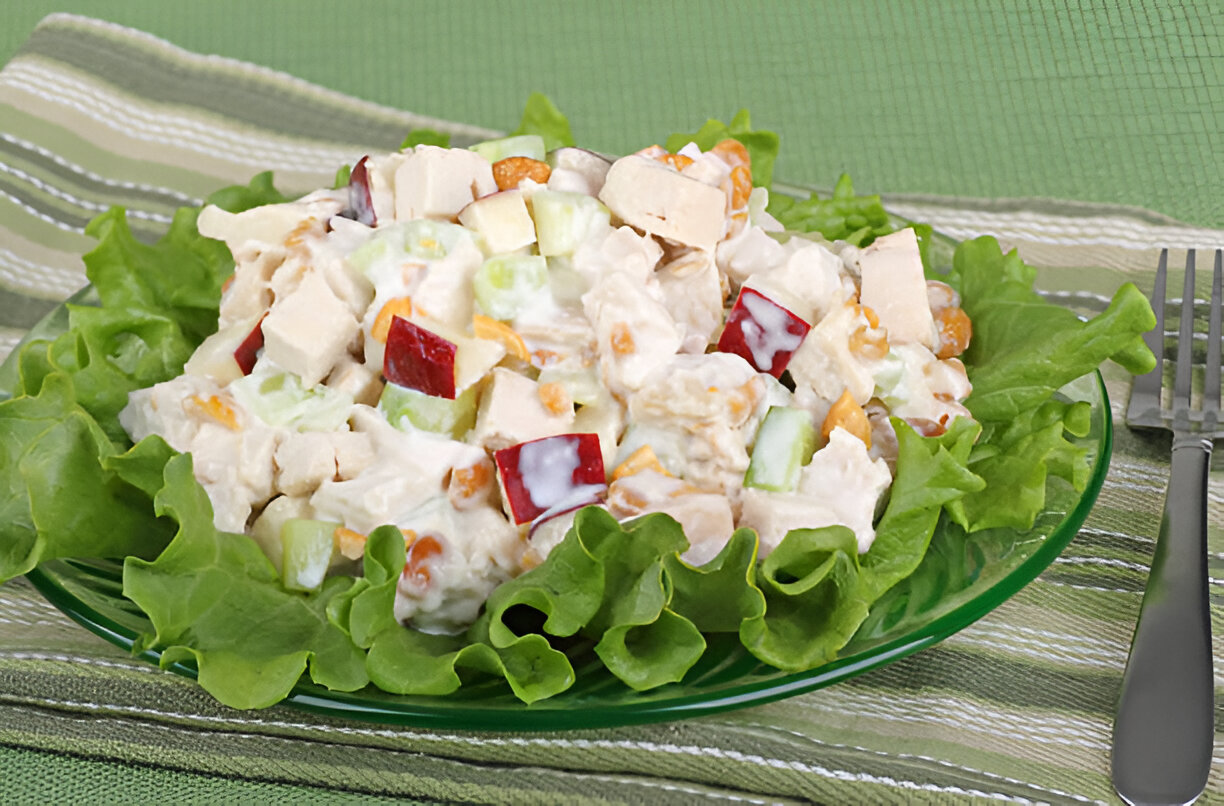 A colorful chicken salad served on a bed of fresh lettuce, featuring diced apples, celery, and nuts.