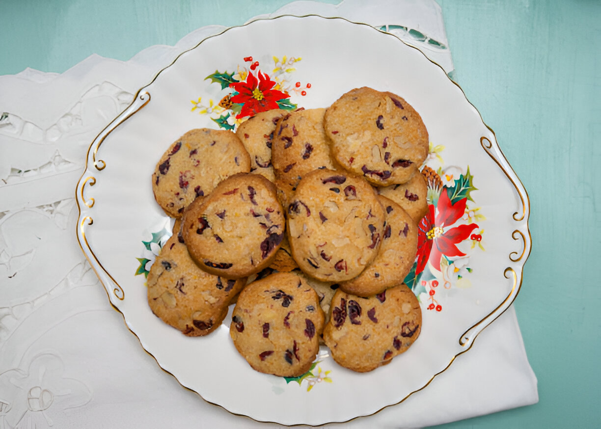 A decorative plate filled with round cookies adorned with cranberries, resting on a white tablecloth.