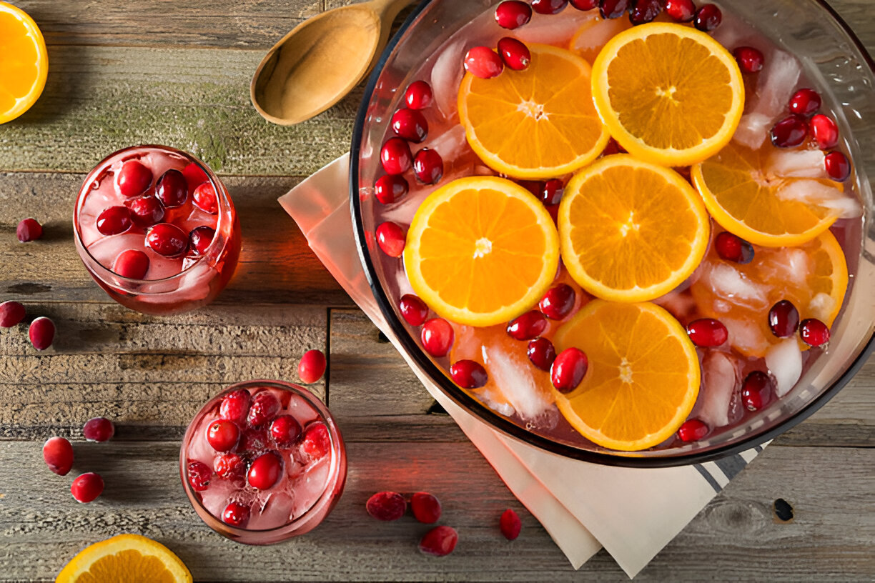 A refreshing punch bowl filled with ice, orange slices, and cranberries on a wooden table.