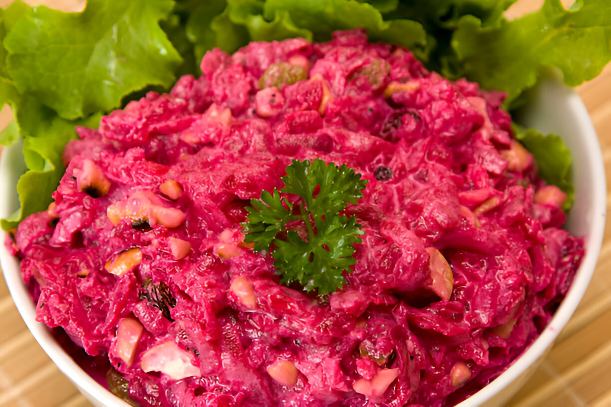 A vibrant pink salad made with beets and nuts, served in a white bowl surrounded by fresh lettuce leaves.