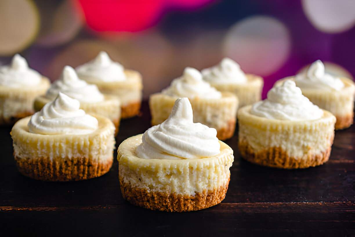 A row of mini cheesecakes topped with whipped cream on a dark wooden surface.