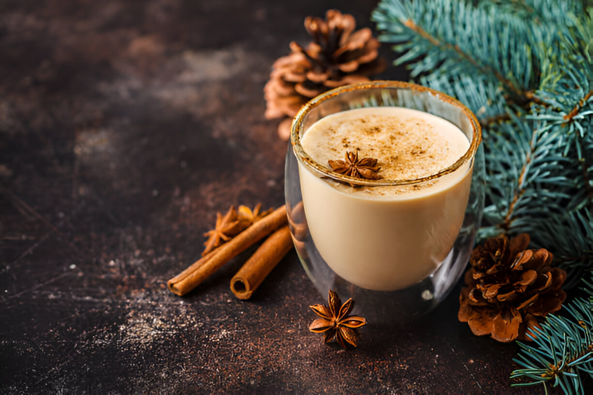 A glass of creamy beverage garnished with star anise, cinnamon sticks, and pine cones on a dark background.