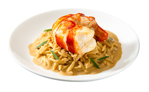 A dish of orzo pasta topped with grilled lobster tail and garnished with herbs on a white plate.