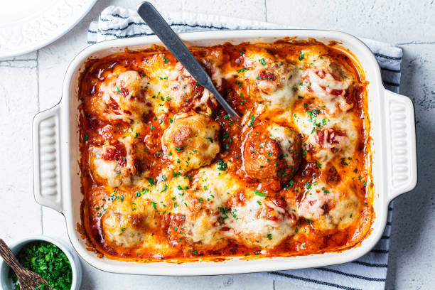 A baked dish of cheesy meatballs in marinara sauce topped with herbs.