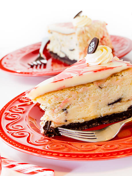 A slice of cheesecake on a red plate with a decorative swirl of frosting and a chocolate garnish, alongside a second slice in the background.