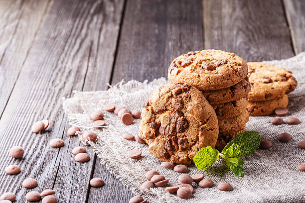 A stack of chocolate chip cookies on a textured cloth with chocolate drops and mint leaves